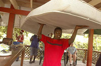 A teen on a retreat carries a mattress on his head in one of the bungalows