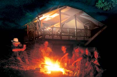 Campers' faces are lit up as they gather around a campfire's glow.
